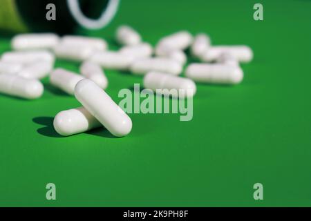 capsule e flacone in pillole bianche su sfondo verde Foto Stock