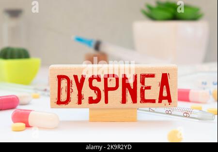 Il testo DISPNEA è scritto su blocco note vicino a uno stetoscopio su sfondo blu. Foto Stock