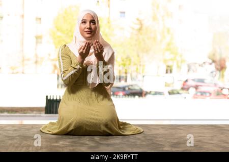 Umile donna musulmana che tiene le mani in su e che prega in pace Foto Stock