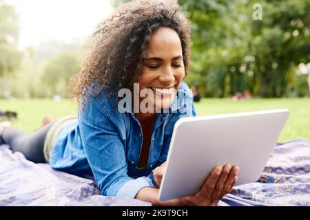Guardare video con aria fresca. Una bella giovane donna che utilizza un tablet in un parco pubblico. Foto Stock