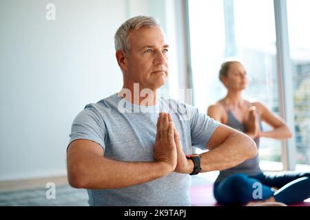 Trovare l'equilibrio, insieme. Un bell'uomo maturo meditare a casa con la moglie sullo sfondo. Foto Stock