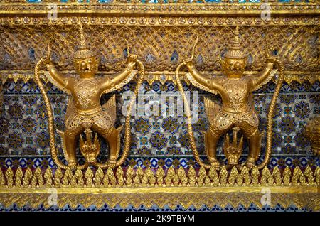 Antiche statue buddiste e guardiani del tempio presso lo Stupa dorato (Phra si Ratana Chedi) accanto al Tempio del Buddha di Smeraldo, Bangkok. Foto Stock