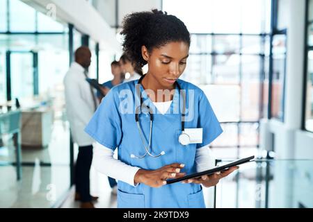 Semplificare le sue mansioni mediche con la tecnologia digitale. Un giovane medico che utilizza un tablet digitale in un ospedale con i suoi colleghi in background. Foto Stock