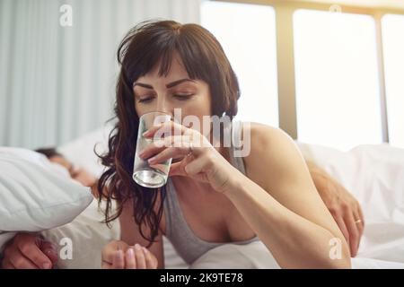 È il momento di svegliarsi. Una giovane donna stanca che si sveglia dopo aver dormito e bevuto acqua mentre era ancora a letto. Foto Stock