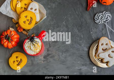 Felice sfondo di Halloween con spazio copia. Tazza rossa con punch tradizionale, diversi biscotti a forma di viso spaventoso, fantasma e ragno, zucche e. Foto Stock