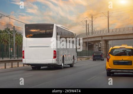 Due autobus bianchi che viaggiano sulla strada asfaltata in paesaggio rurale al tramonto con nuvole drammatiche Foto Stock