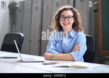 Giovane donna felice insegnante on-line seduto alla scrivania con un computer portatile. Verticale Foto Stock