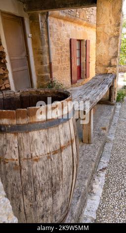 n vecchio barile di legno, panca fatta a mano e tronchi di fuoco di legno sotto un portico costruito in pietra Foto Stock