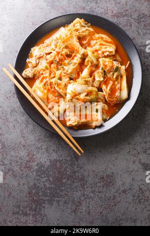 Mangiare cavolo kimchi in una ciotola con bacchette, primi piatti coreani in un piatto nero su un tavolo. Vista verticale dall'alto Foto Stock