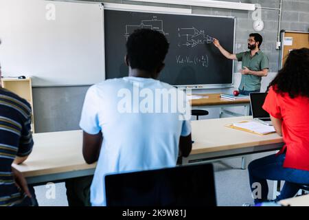 Giovane insegnante di scuola superiore maschile che insegna lezioni elettroniche agli studenti Foto Stock