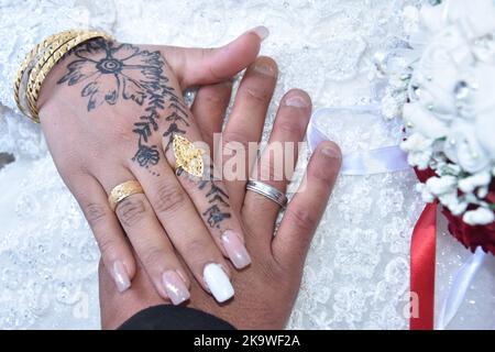 Mani di sposi novelli con anelli di nozze e bouquet nuziale. L'henné che attinge sulla pelle, non un tatuaggio Foto Stock