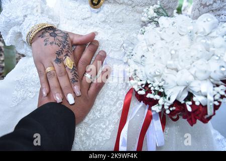 Mani di sposi novelli con anelli di nozze e bouquet nuziale. L'henné che attinge sulla pelle, non un tatuaggio Foto Stock