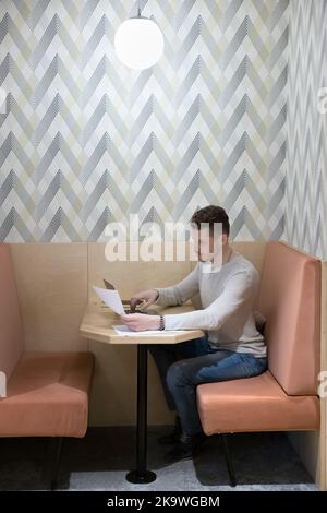 Un uomo d'affari serio e focalizzato che scrive sul laptop contiene documenti, preparando il rapporto Foto Stock