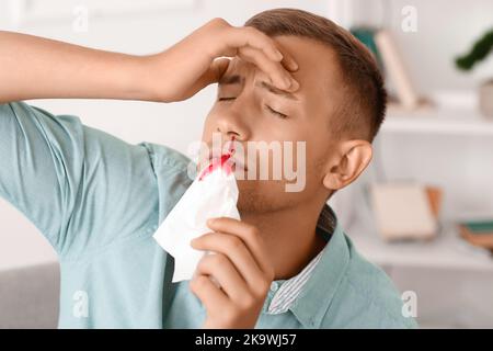 Giovane uomo con sangue di naso e tessuto a casa, primo piano Foto Stock