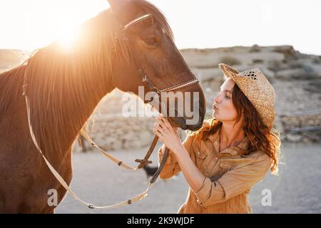 Giovane donna contadina che ha momento tenero baciando il suo cavallo al ranch fattoria - Focus on Face Foto Stock