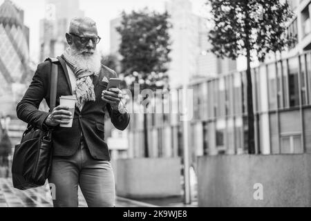 Dirigente d'affari che usa il telefono cellulare mentre cammina per lavorare con la città in background - Focus Face - editing in bianco e nero Foto Stock