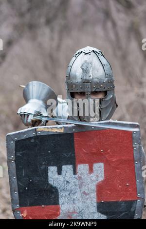Nobile guerriero. Ritratto di un guerriero o cavaliere medeivale in armatura e casco con scudo e spada in posa isolata su sfondo scuro. Foto Stock