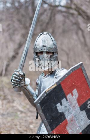 Nobile guerriero. Ritratto di un guerriero o cavaliere medeivale in armatura e casco con scudo e spada in posa isolata su sfondo scuro. Foto Stock