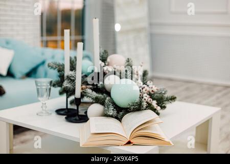 Un libro aperto sul tavolo, candele e una corona di Natale nel soggiorno Foto Stock