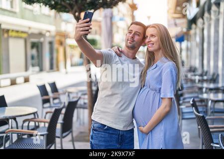 Coppia uomo e donna che si aspettano il bambino fare selfie da smartphone alla terrazza del bar Foto Stock