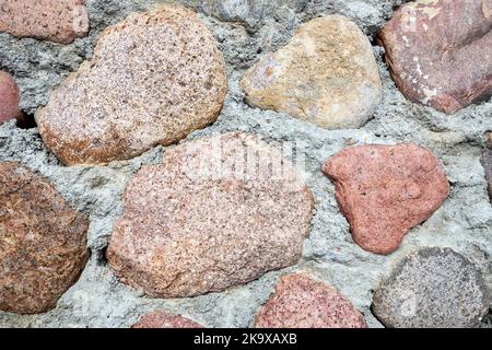 Grandi pietre rosse arancio marrone con fondo in cemento. Antico frammento di mura del castello lastricato di ciottoli. Foto Stock