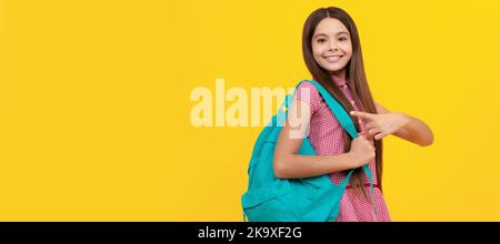 felice ragazza teen scuola punta dito sullo zaino su sfondo giallo. Ritratto della studentessa scolastica, intestazione banner studio. Faccia del bambino della scuola Foto Stock