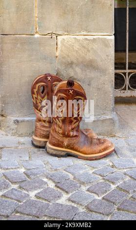 Paesaggio all'aperto che mostra un paio di stivali da cowboy scappati su un terreno acciottolato di fronte a un muro di arenaria Foto Stock