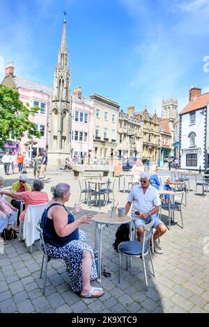 La città di Glastonbury nel Somerset con un caffè di strada sulla piazza del mercato e la Croce del mercato. Foto Stock