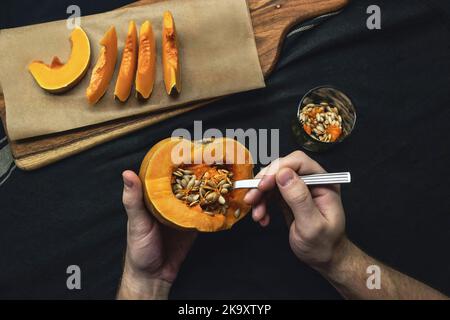 Mani maschili che rimuovono i semi con il cucchiaio da una zucca tagliata di fresco su fondo nero Foto Stock