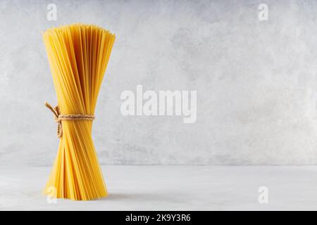 Spaghetti di pasta cruda su sfondo grigio. Mazzo verticale di spaghetti non cotti legati con spago. Spazio di copia Foto Stock