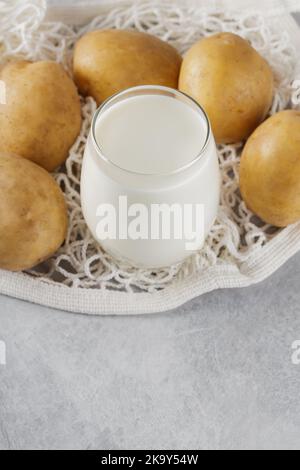 Latte di patata e patate crude in un sacchetto a rete. Prodotto sostitutivo del latte a base di piante e privo di lattosio. Latte vegetale e concetto di stile di vita sostenibile Foto Stock