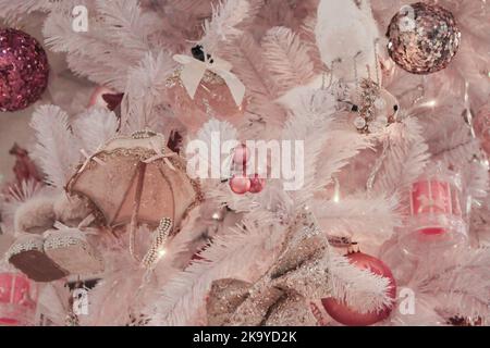 Albero di Natale bianco e rosa con giocattoli: Palline lucenti, ombrello, archi. Delicato sfondo di Natale. Foto Stock