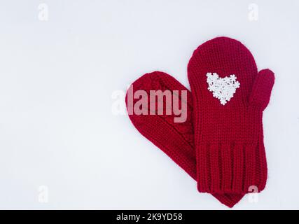 Due guanti rossi a maglia si trovano l'uno con fiocchi di neve bianchi a forma di cuore. Sfondo bianco, isolato. Concetto di Natale, inverno, lo Foto Stock