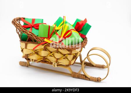 Santa slitta in vimini vecchio stile con regali di Natale avvolti in carta verde con nastro rosso. Foto Stock