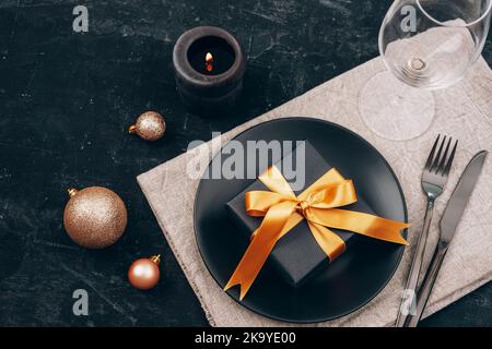 Tabella di Natale e Capodanno in nero. Piatto nero, posate, confezione regalo, candela, wineglass e giocattoli. Vista dall'alto. Foto Stock