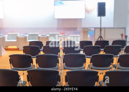 Super sala conferenze con sedie nere, illuminazione colorata e schermo vuoto Foto Stock