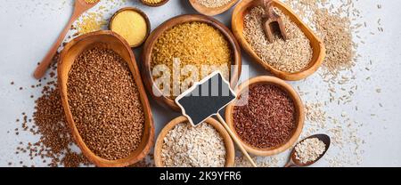 Varietà di grani. Cereali assortiti riso bianco, marrone e rosso, grano saraceno, miglio, semole di mais, quinoa e bulgur in ciotole di legno. Crisi dell'approvvigionamento alimentare. Foto Stock