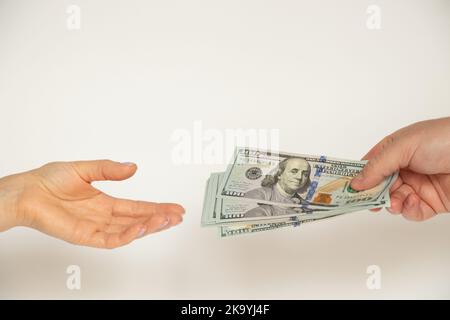 Una mano dell'uomo dà cento dollari fatture ad una donna su uno sfondo bianco, dà e prende i soldi, il commercio e l'investimento Foto Stock