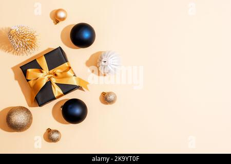 Scatola regalo nera con nastro dorato e baubles di Natale su sfondo beige. Vista dall'alto, disposizione piatta, spazio di copia. Foto Stock