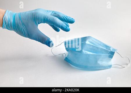 Una persona in un guanto di protezione blu raggiunge per una maschera medica di protezione. Mezzi di protezione antivirale e antibatterica Foto Stock