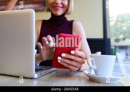 Foto ravvicinata di una donna caucasica che usa lo smartphone per lavorare a distanza in un bar Foto Stock