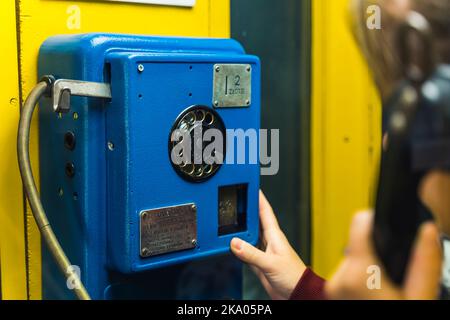 Persona non riconoscibile caucasica che tiene il ricevitore nero in una mano e tocca il telefono blu scuro in una cabina con l'altra. Processo di comunicazione nei primi inizi. Scatto in interni. Foto di alta qualità Foto Stock