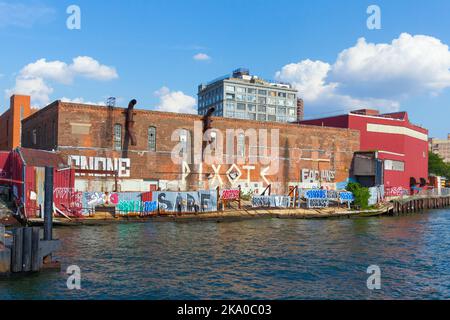 Graffiti lungo l'East River Waterfront sotto un edificio di loft a Brooklyn, New York, USA. Foto Stock