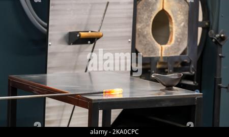 Utilizzando un punzone di metallo per rotolare un vetro, riunirsi su una piastra di acciaio della marver. Foto Stock