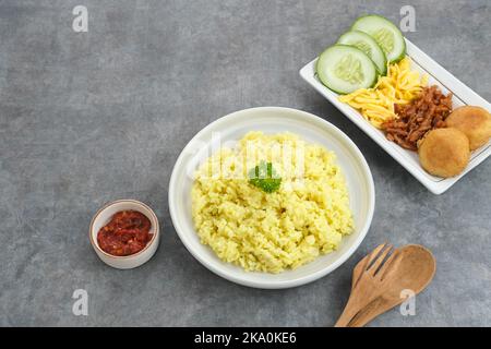 Nasi Kuning, cibo tradizionale indonesiano, a base di riso cotto con latte di curcuma e cocco e spezie, servito con vari contorni Foto Stock