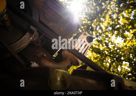 Motore diesel di un trattore retrostante con una trasmissione a cinghia in primo piano. Vista parziale dal basso con luce solare Foto Stock