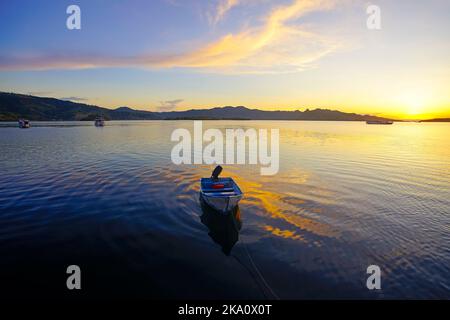 Piccola barca solitaria con bella alba e riflesso in acqua Foto Stock