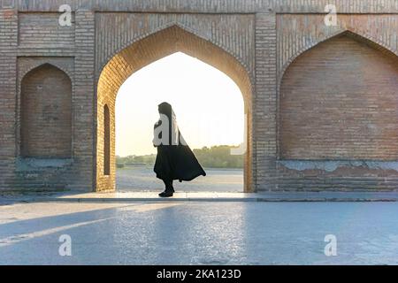 Donna islamica con foulard tradizionale e vestito sul ponte Khaju a Isfahan, Iran. Silhouette inidentificabile come la forma di una donna iraniana Foto Stock