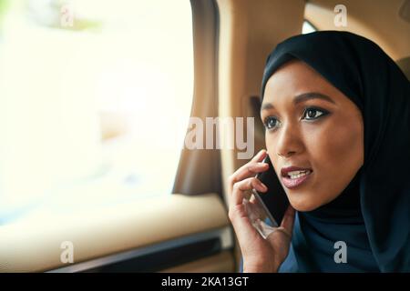 Grazie per aver chiamato. Una giovane donna d'affari concentrata che parla sul suo telefono cellulare mentre è seduto sul retro di un'auto sul suo cammino verso il lavoro. Foto Stock