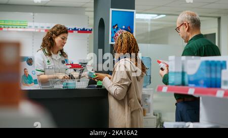 Farmacista aiutare la donna afroamericana a comprare farmaci e cure sanitarie al banco farmacia. Dipendente scansione scatole di pillole e vitamine per vendere farmaci. Foto Stock
